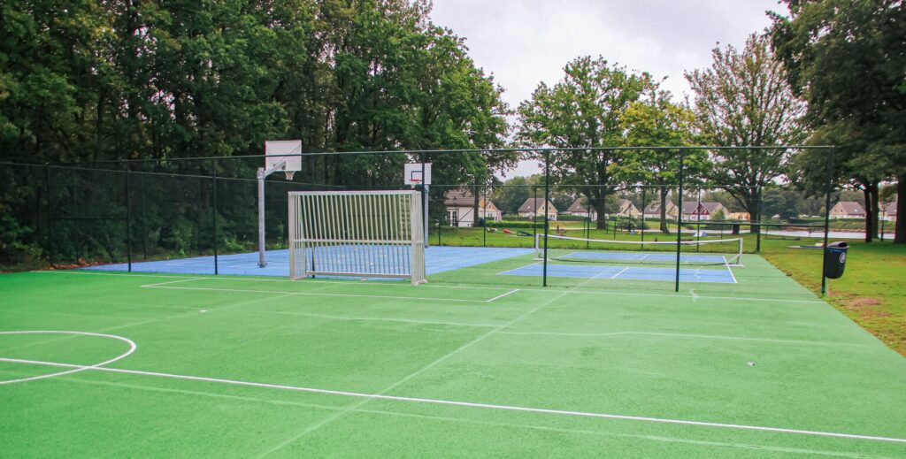 Foto van de vernieuwde sportvelden, met op de voorgrond het voetbalveld en op de achtergrond het basketbalveld en het pickleballveld.